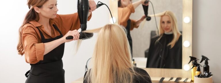Fryzjerka susząca włosy klientki w salonie fryzjerskim przy lustrze z żarówkami