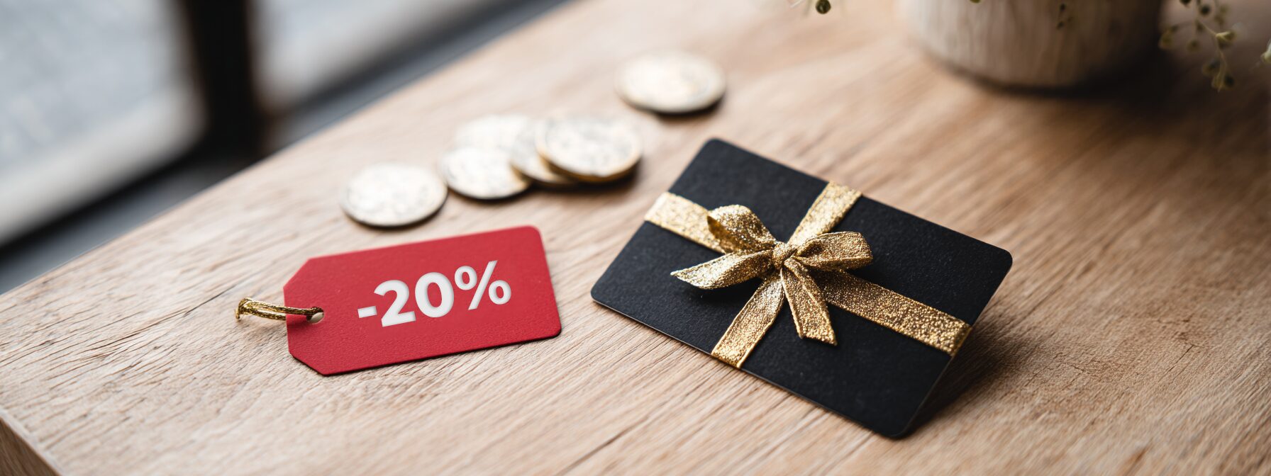 Flat lay przedstawiający porównanie: po lewej czerwona etykieta z rabatem i monety, po prawej elegancka czarna karta podarunkowa ze złotą wstążką na drewnianym stole